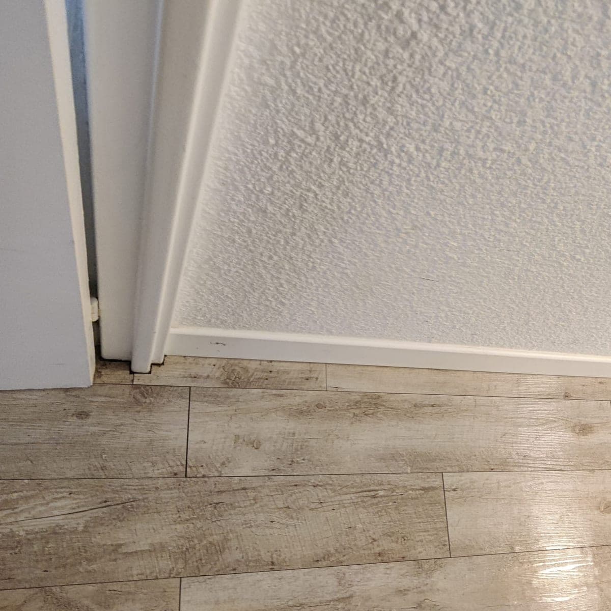 Plinthe blanche, sol imitation bois brillant et pied d'huisserie, nets, le long d'un mur crépi