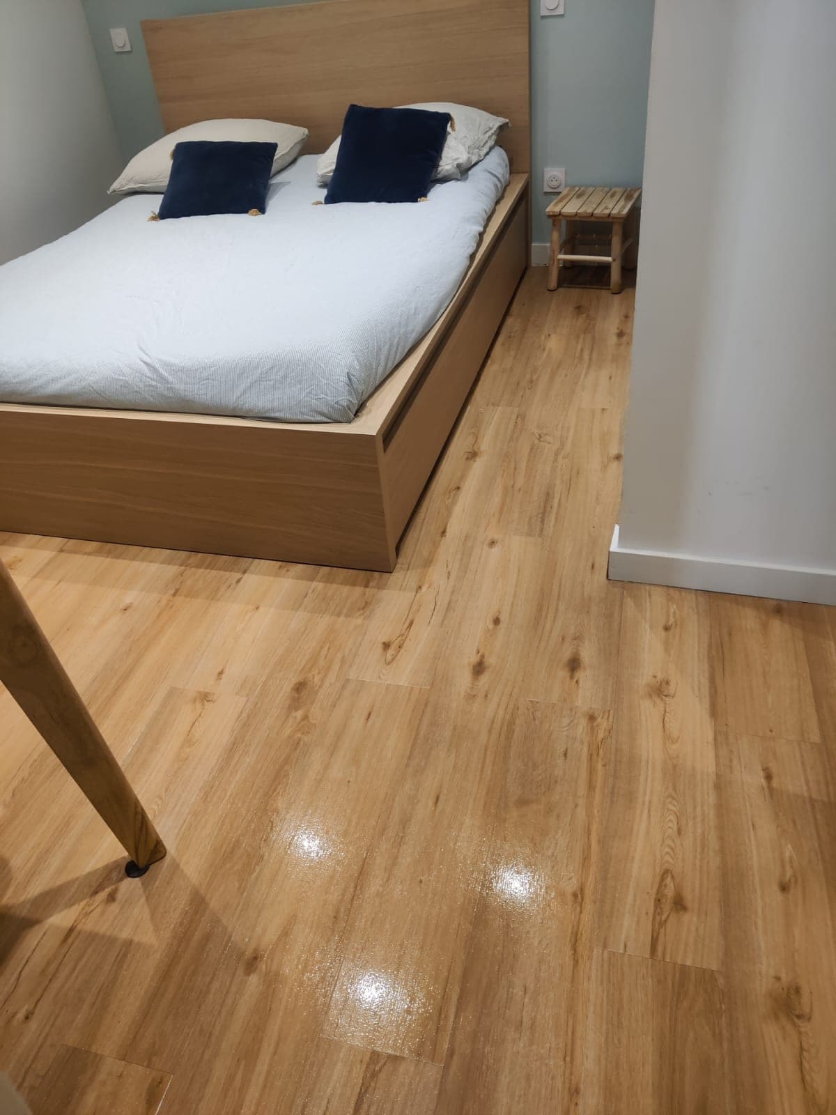 Chambre avec lit à draps blancs et parquet clair brillant