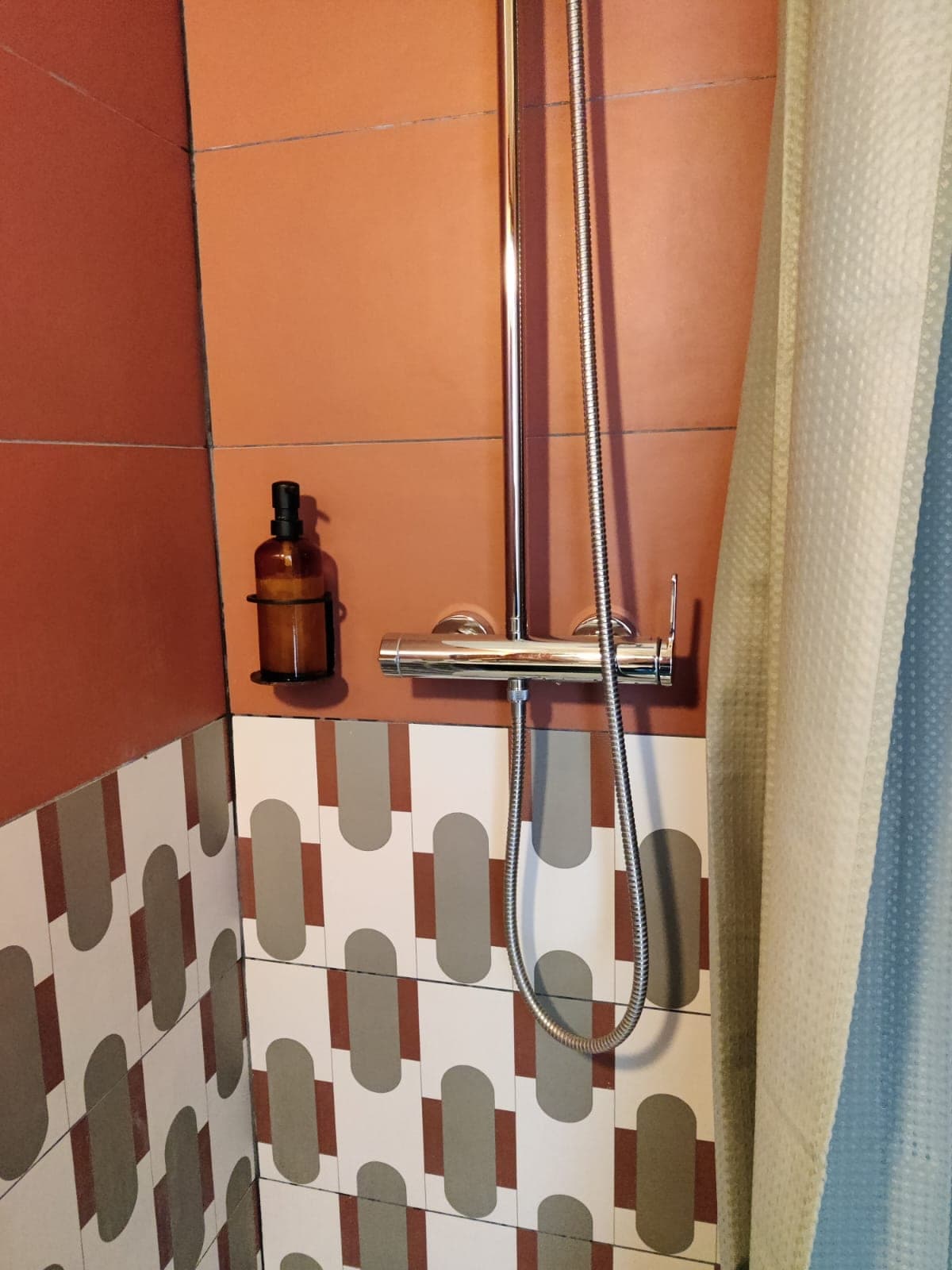 Douche à carreaux terracotta et motifs gris, mitigeur chromé et rideau, propres