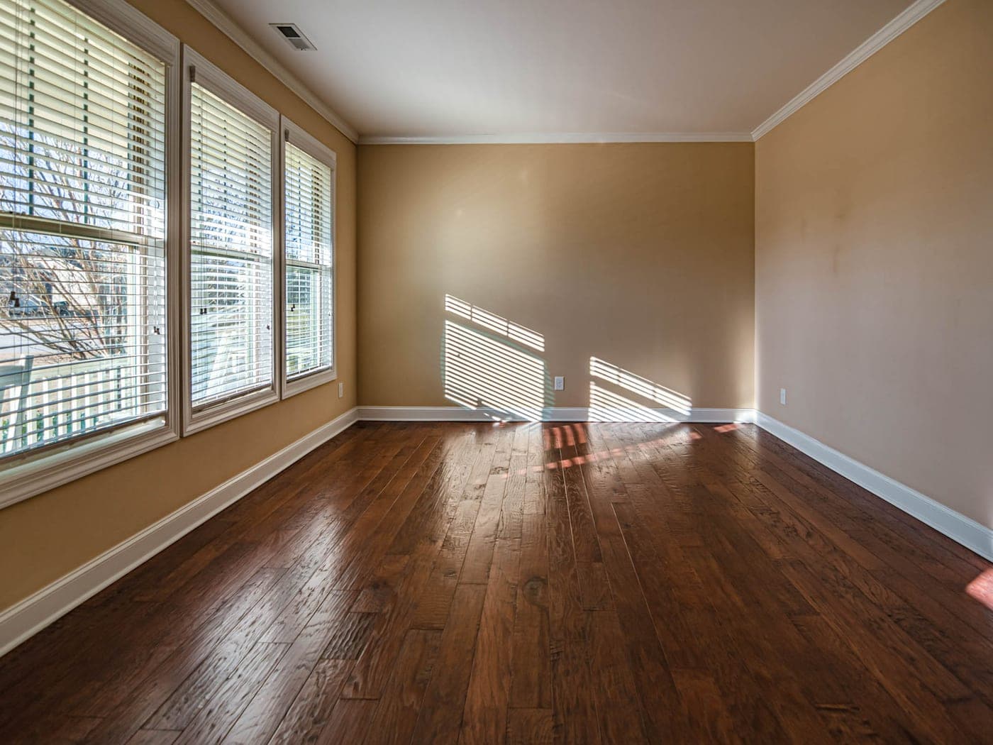 Pièce vide au parquet foncé, grandes fenêtres à persiennes et lumière franche